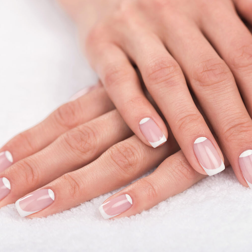 A woman 's hands with french manicure on top of her fingers.