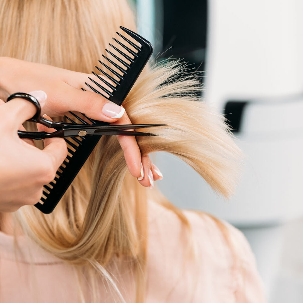 A woman is cutting her hair with scissors.